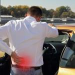 image of man with back pain standing with car