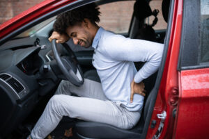 Male experiencing back pain after a long drive in his car.