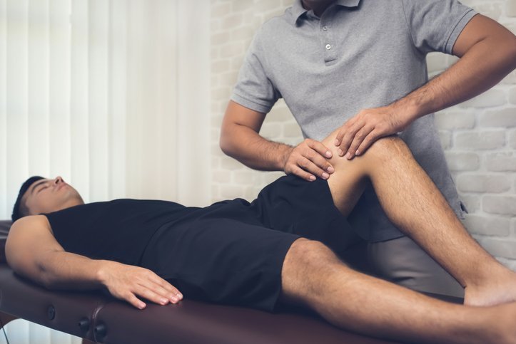 Physical therapist working on a knee of a man lying on a table. 