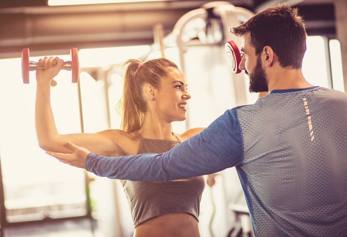 Personal trainer helping a woman to improve her arm position while lifting dumbbells