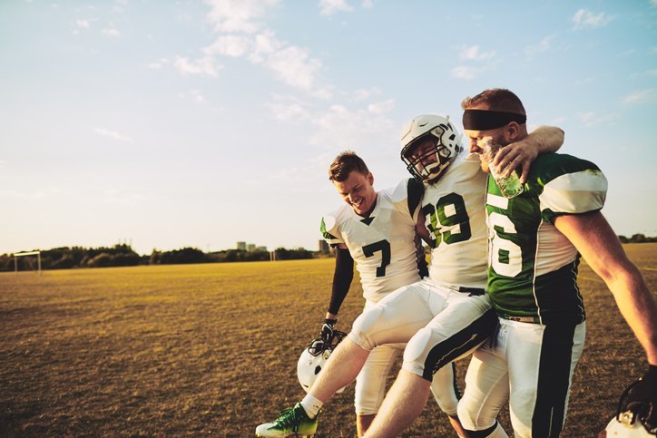 football players assisting teammate off the field after an injury