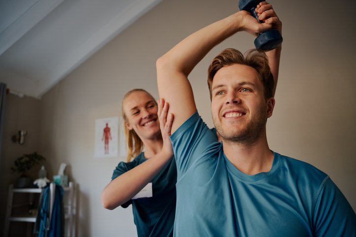 Physical therapist stretching a man's Right shoulder while he is sitting
