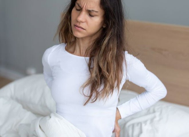 Woman getting out of bed in the morning with joint stiffness in the her lower back with pain