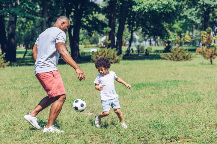 father practicing soccer with child outside on the grass